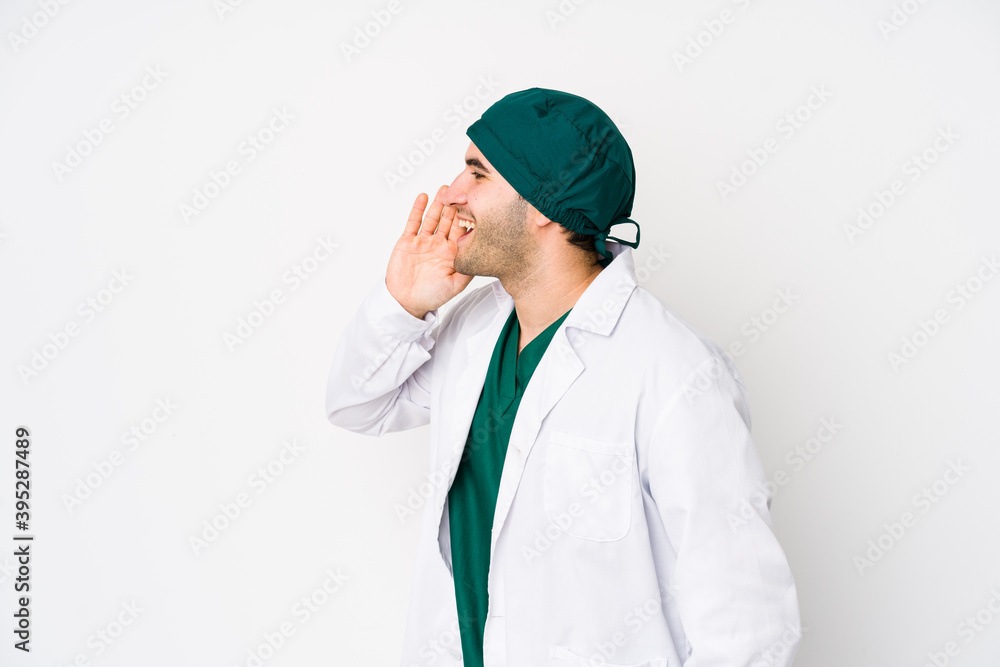 Young surgeon man isolated on white background shouting and holding palm near opened mouth. Young surgeon man isolated on white background shouting and holding palm near opened mouth.