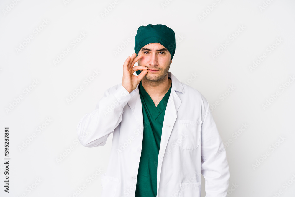 Young surgeon man isolated on white background with fingers on lips keeping a secret. Young surgeon man isolated on white background with fingers on lips keeping a secret.