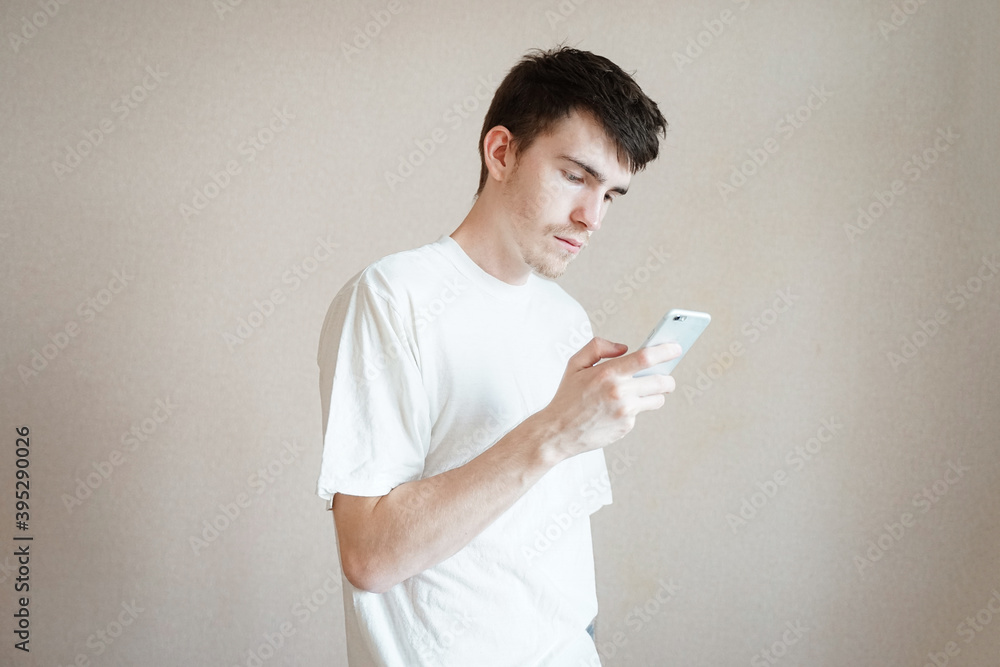 teenager with black hair and a white t-shirt, holds a phone in his hand, looks into a smartphone, addiction teenager with black hair and a white t-shirt, holds a phone in his hand, looks into a smartphone, addiction