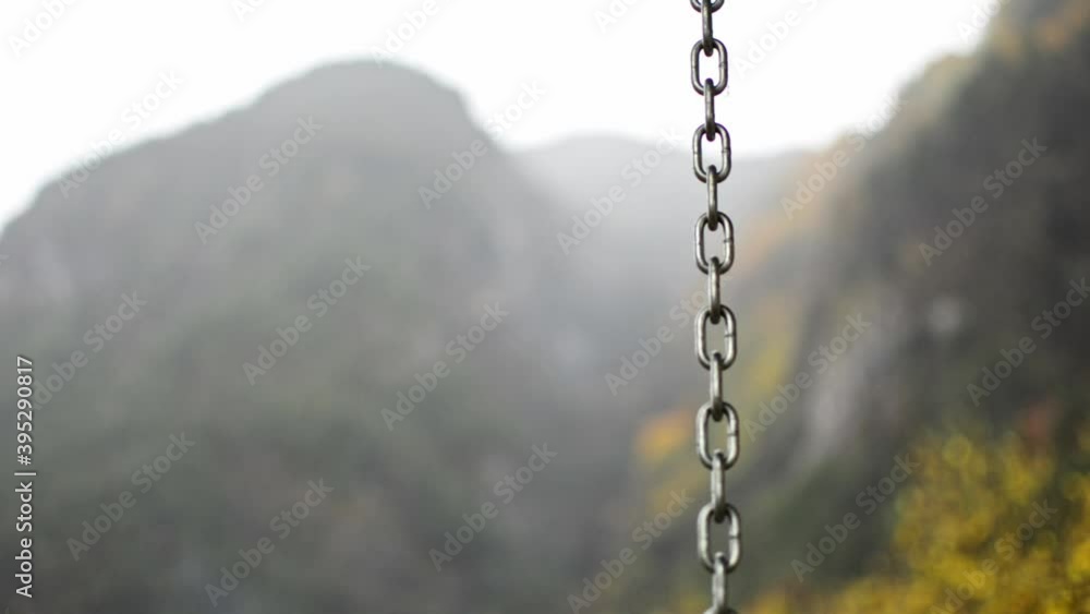 a chain from a swing chair dancing in the rain during a cold autumn day, the blurry mountains behind offer a beautiful scene; slowly focusing away from the chain, rain and trees are revealed a chain from a swing chair dancing in the rain during a cold autumn day, the blurry mountains behind offer a beautiful scene; slowly focusing away from the chain, rain and trees are revealed