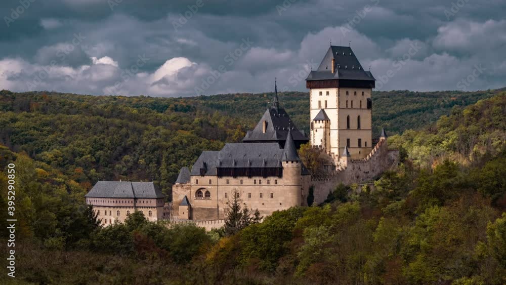 Aerial view of the beautiful Karlštejn Castle, towering solemnly on the hill surrounded by the dense green forest. Heavy gray-blue clouds rush above the gothic castle. Aerial view of the beautiful Karlštejn Castle, towering solemnly on the hill surrounded by the dense green forest. Heavy gray-blue clouds rush above the gothic castle.