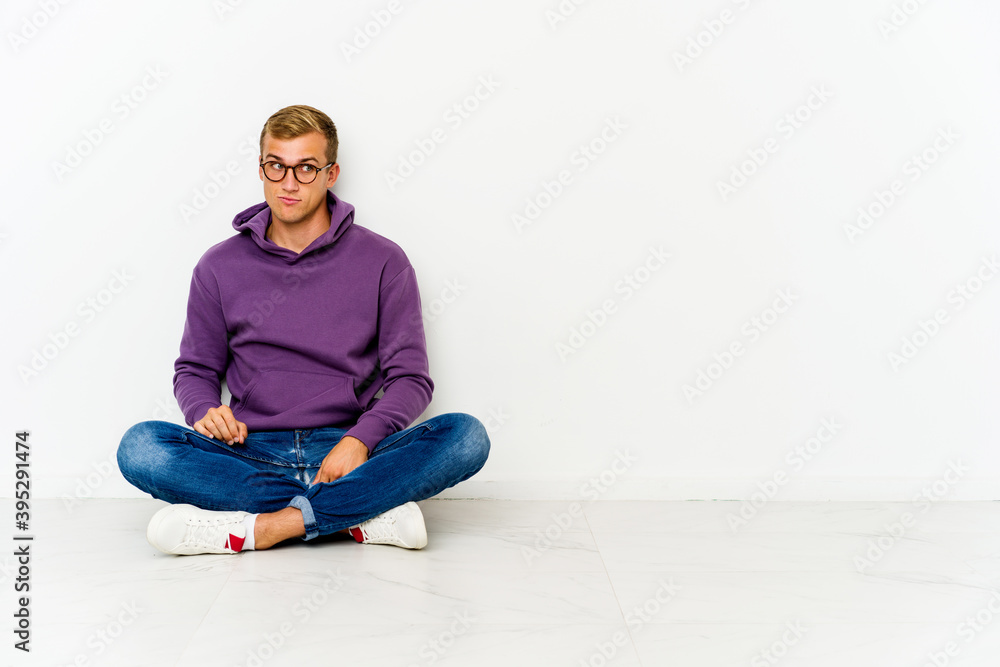 Young caucasian man sitting on the floor confused, feels doubtful and unsure. Young caucasian man sitting on the floor confused, feels doubtful and unsure.