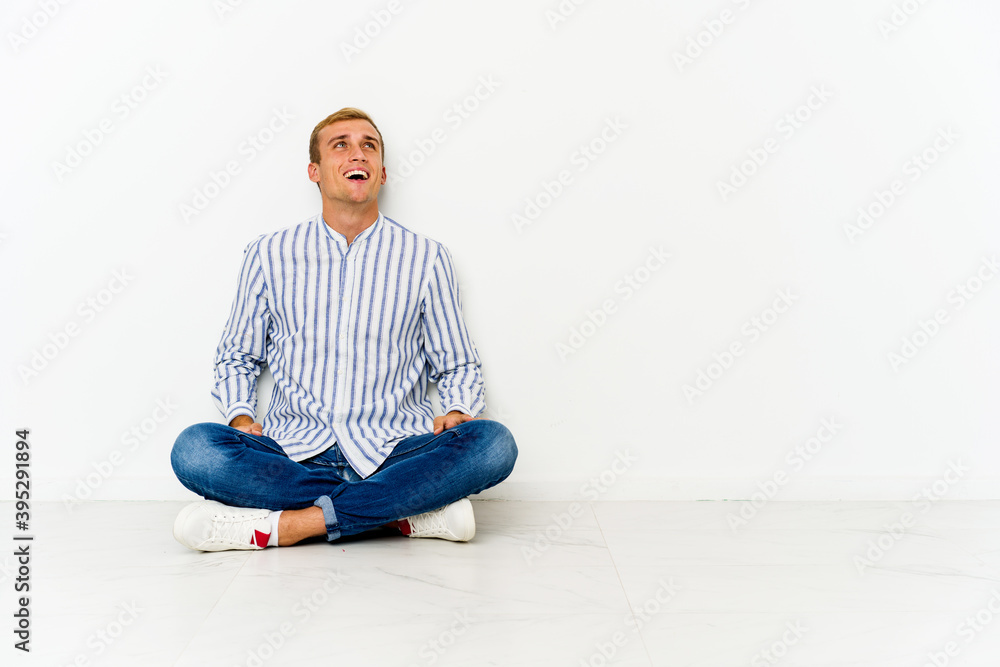 Young caucasian man sitting on the floor relaxed and happy laughing, neck stretched showing teeth. Young caucasian man sitting on the floor relaxed and happy laughing, neck stretched showing teeth.