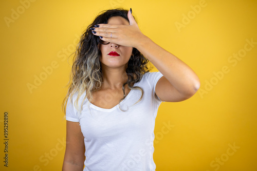 Young beautiful woman wearing casual white t-shirt over isolated yellow background serious and covering her eyes with her hand