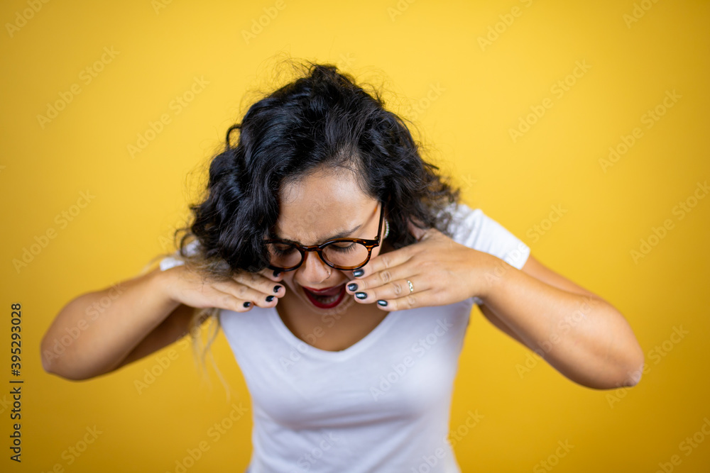 Young beautiful woman wearing casual white t-shirt over isolated yellow background shouting and screaming loud down with hands on mouth Young beautiful woman wearing casual white t-shirt over isolated yellow background shouting and screaming loud down with hands on mouth