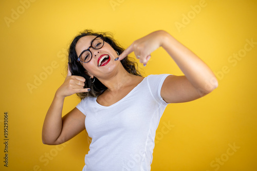 Young beautiful woman wearing casual white t-shirt over isolated yellow background doing the “call me” gesture with her hands.