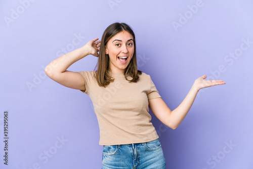 Young caucasian woman holds copy space on a palm, keep hand over cheek. Amazed and delighted.
