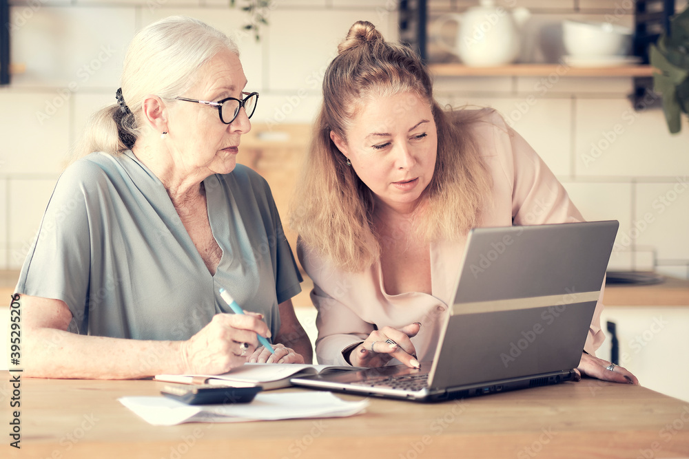 Senior woman using laptop for websurfing in her kitchen. middle-aged daughter helps her mother with documents. Mature lady sitting at work typing a notebook computer in an home office. Senior woman using laptop for websurfing in her kitchen. middle-aged daughter helps her mother with documents. Mature lady sitting at work typing a notebook computer in an home office.