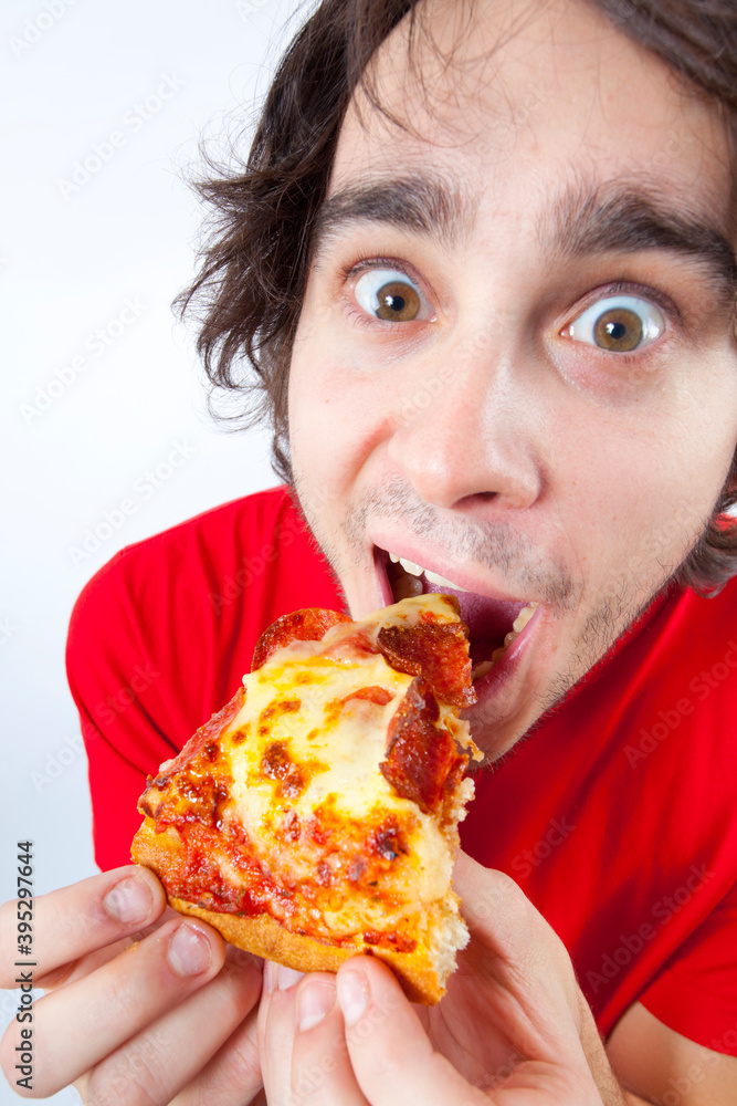 Fish eye photo of young man with dark hair eating a slice of pepperoni pizza