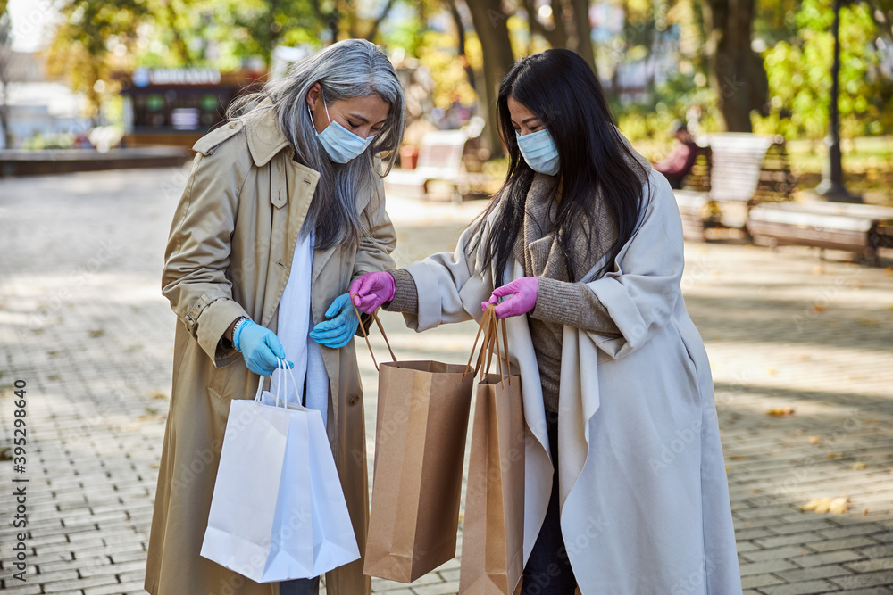 Female friends in medical masks looking inside shopping bag