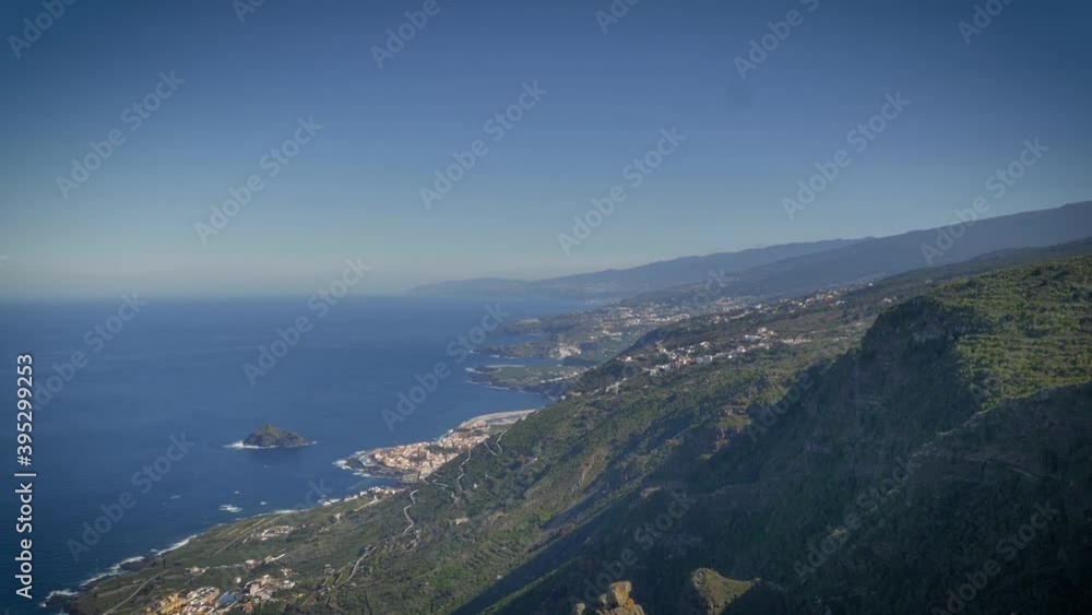 Haze on horizon. Aerial view of Tenerife coast with steep green slopes meeting the blue sea. Cliffs along rugged shoreline of popular tourist destination. Holiday and vacation in Europe. Haze on horizon. Aerial view of Tenerife coast with steep green slopes meeting the blue sea. Cliffs along rugged shoreline of popular tourist destination. Holiday and vacation in Europe.