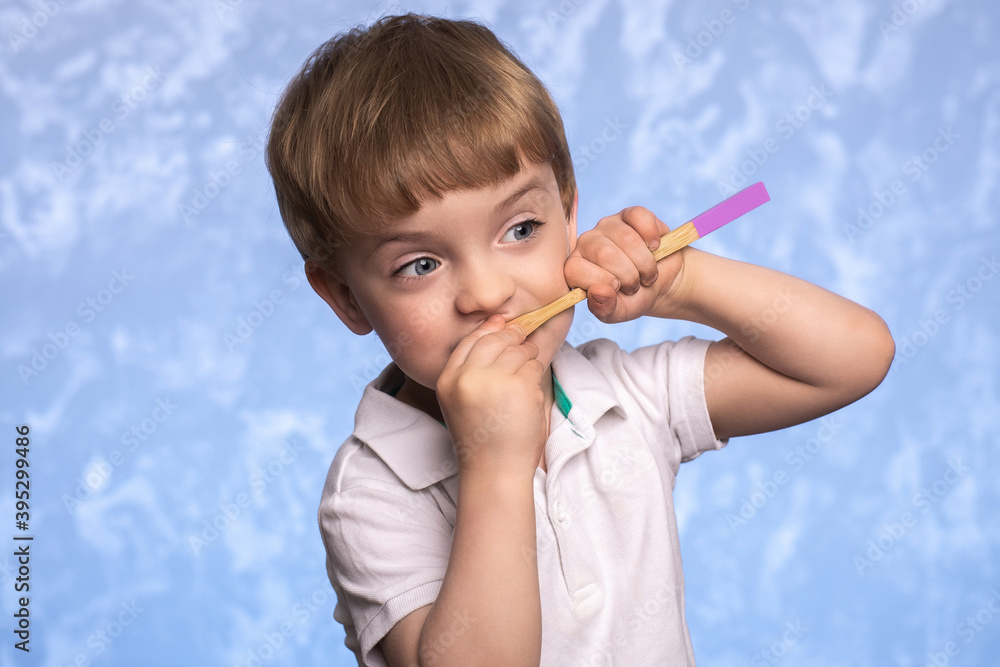 little child brushes teeth with a bamboo toothbrush in the bathroom on a blue texture background. horizontal photo. ecologicaly clean. morning hygiene concept. little child brushes teeth with a bamboo toothbrush in the bathroom on a blue texture background. horizontal photo. ecologicaly clean. morning hygiene concept.