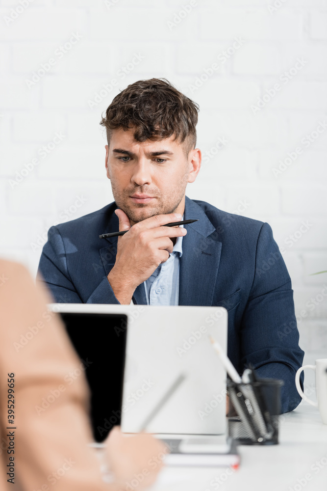businessman looking at laptop, while sitting at table in office on blurred foreground businessman looking at laptop, while sitting at table in office on blurred foreground