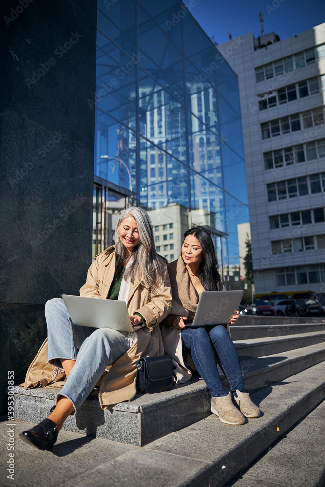 Two beautiful women using modern laptops outdoors
