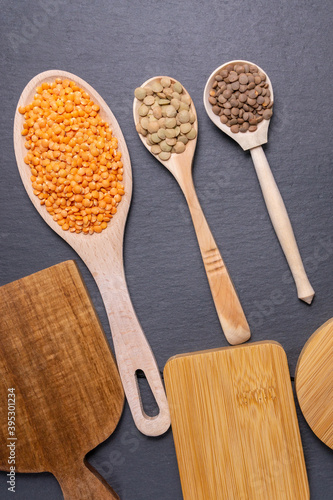 dry orange, red, green lentils in wooden spoons on a black background top view, flat lay