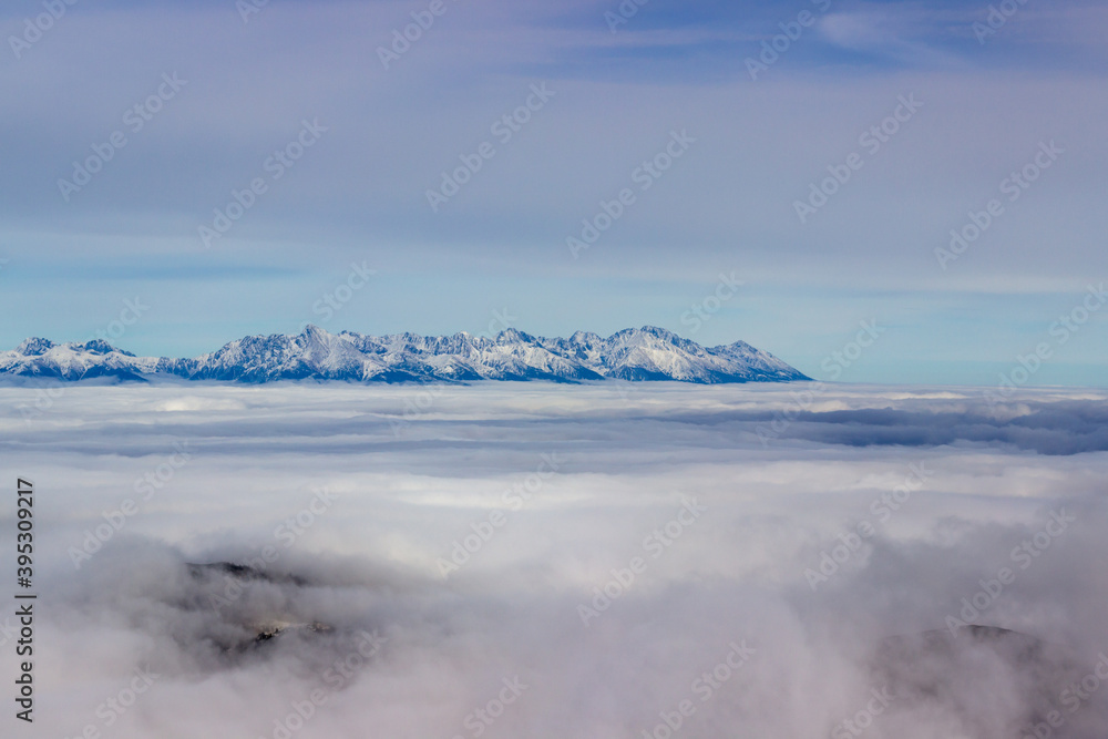 Sun is shining on top of the low Tatry at foggy autumn day looking into mountain tops of the high Tatry in distance. Mountain tops in white fog and blue background Sun is shining on top of the low Tatry at foggy autumn day looking into mountain tops of the high Tatry in distance. Mountain tops in white fog and blue background