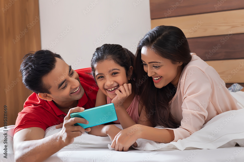family relaxing on bed together during the day with a smart phone family relaxing on bed together during the day with a smart phone
