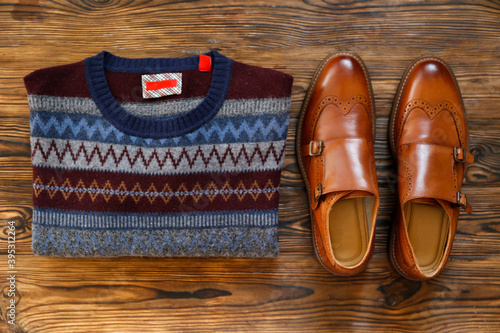 Top view shot of folded sweater with festive pattern and brown men's shoes. Set of male clothing. Close up, copy space, flat lay, background.