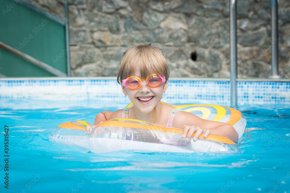 a little girl in pink swimming glasses takes a dip in the pool with a swimming circle