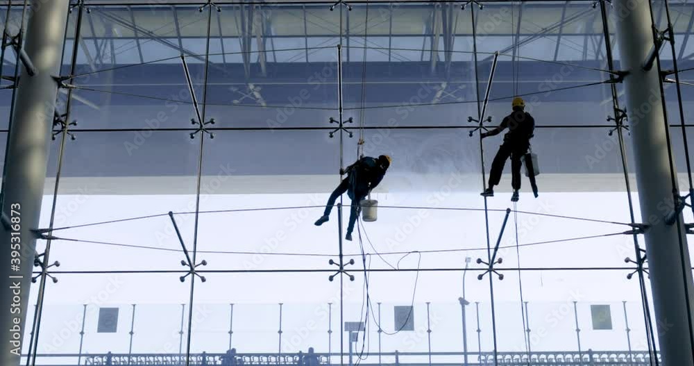Two male workers cleaning windows on a high glass Two male workers cleaning windows on a high glass