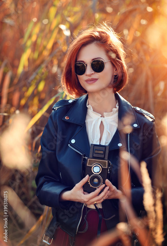 Beautiful young redhaired woman with a retro camera. Autumn sunny day photo