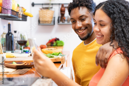 Happy young couple looking the recipe on the tablet. Beautiful young couple smiling preparing healthy food in kitchen at home. Technology, love and food concept.