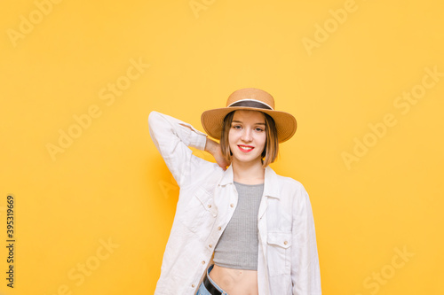 Pretty positive girl in a white shirt and sun hat stands on a yellow background, looks into the camera with a smile on her face. Hiker girl in summer clothes posing on yellow background. Isolated.