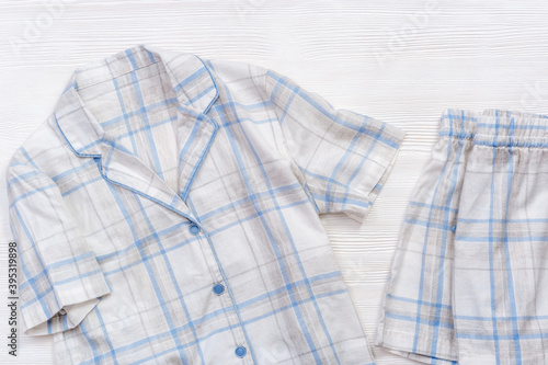 White cotton pajamas with blue checks or stripes, on a white wooden background. Nightwear for sleeping. Top view.