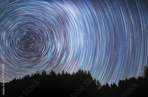 Beautiful starry sky with star trails behind the trees silhouette. Space background. Abstract long exposure background. 