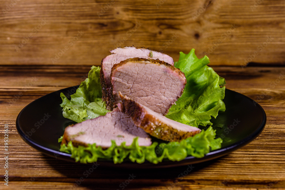 Slices of baked pork meat and lettuce leaves on a black plate Slices of baked pork meat and lettuce leaves on a black plate