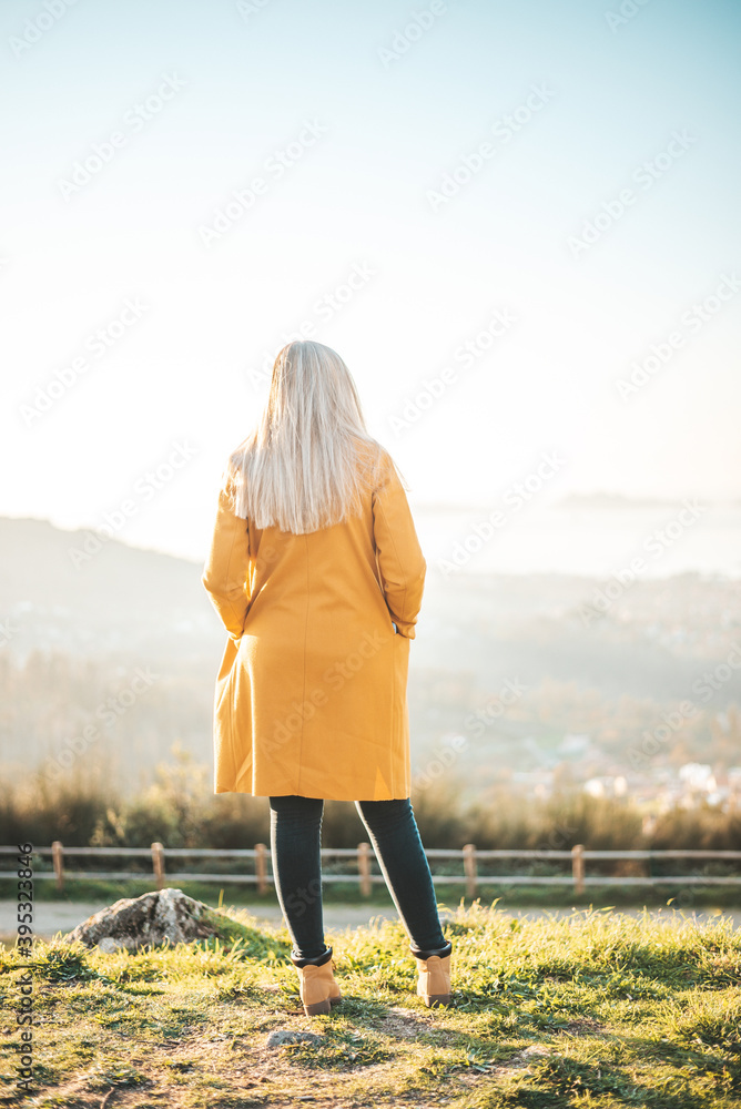 Woman on a yellow coat sitting on a bench contemplating the landscape