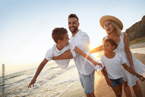 Happy family having fun on sandy beach near sea at sunset