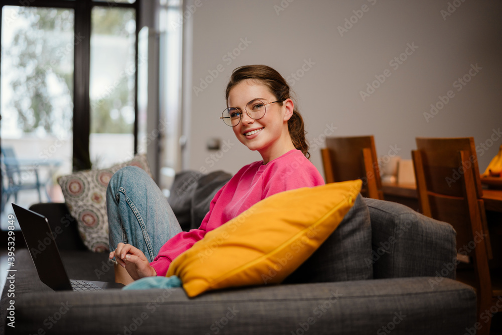 Beautiful smiling girl working with laptop while sitting on couch Beautiful smiling girl working with laptop while sitting on couch