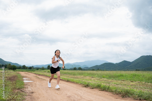 Happy Funny little asian girl fitness woman running at morning tropical forest trail. Athletic young child running in the nature. Healthy lifestyle.