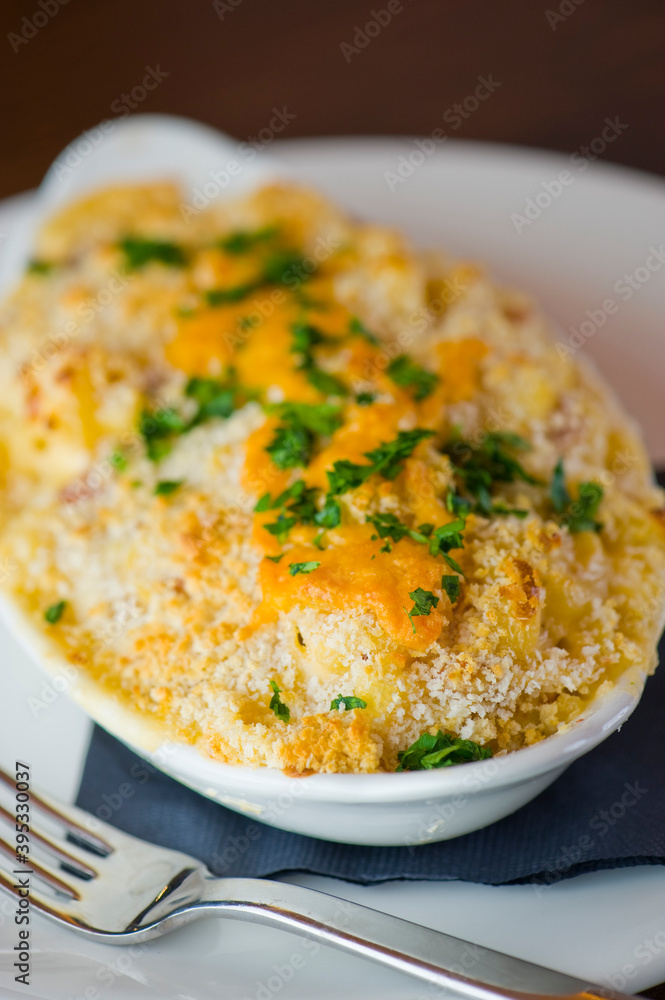 Potatoes au gratin. Potatoes baked in butter, cheese cream sauce, garnished with scallions, parsley and served in cast iron skillet. Classic American restaurant or French bistro side dish.