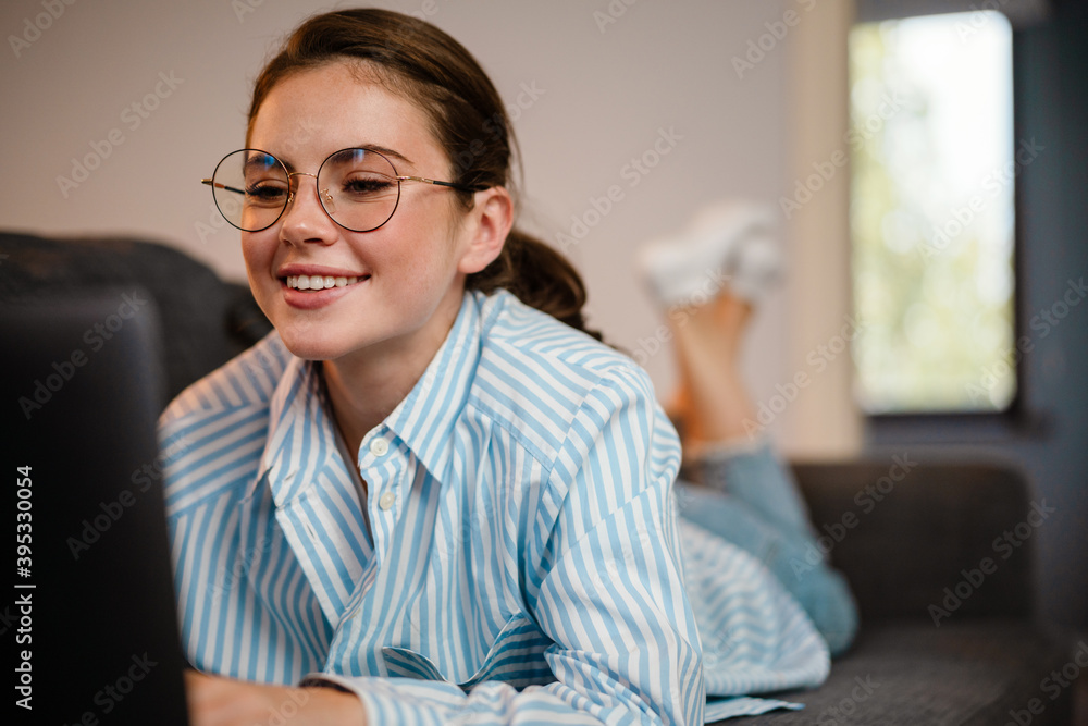 Beautiful smiling girl working with laptop while lying on couch Beautiful smiling girl working with laptop while lying on couch