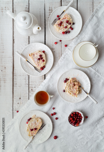Table set for tea with meringue roulade, fresh cranberries, tea cups on Nordic style wooden background