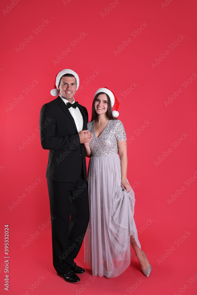 Beautiful happy couple in Christmas hats on red background