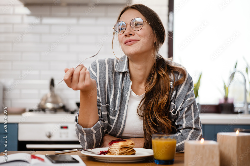 Smiling beautiful woman eating pancakes while having breakfast - obrazy, fototapety, plakaty 