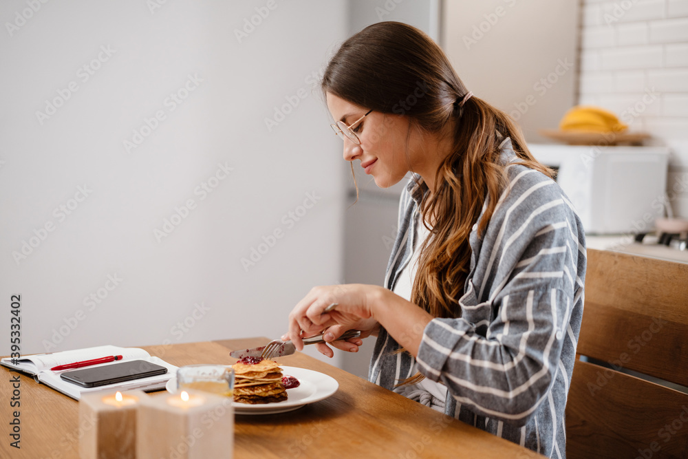 Smiling beautiful woman eating pancakes while having breakfast Smiling beautiful woman eating pancakes while having breakfast