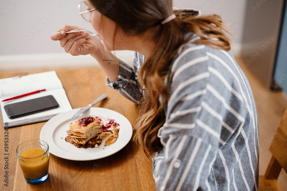 Young beautiful woman eating pancakes while having breakfast