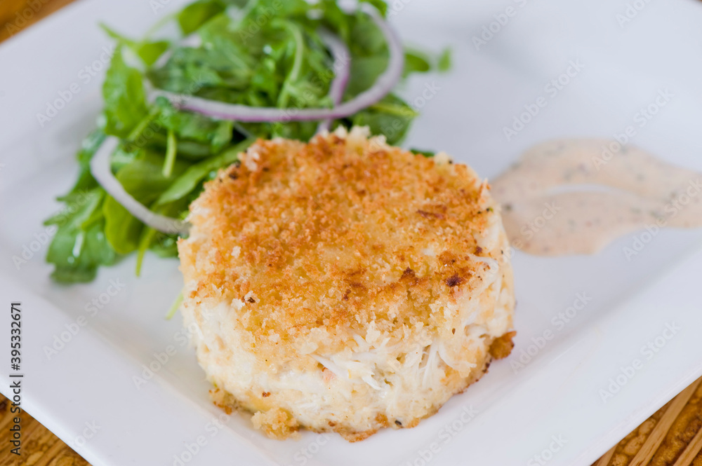 Crab cake. Crab served with spicy rémoulade sauce on top of a mixed green salad. Jumbo crab meat mixed with garlic, onions, spices & fried in butter. Classic American restaurant appetizer.