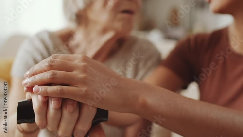 Close up selective focus shot of hands of young woman holding hands of senior grandmother while sitting with her at home and speaking photo