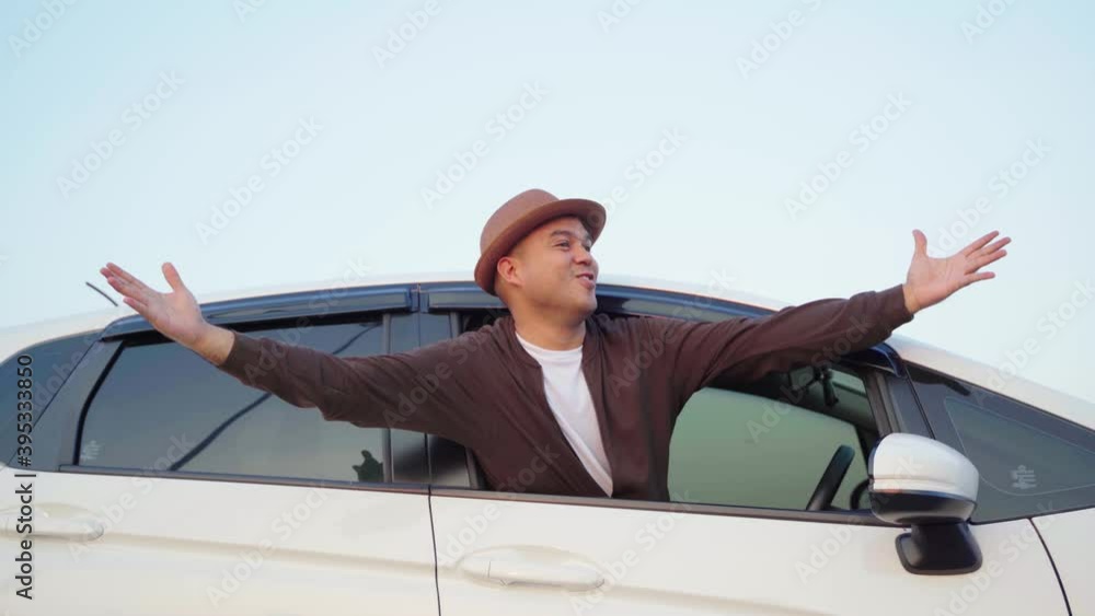 A young Asian man sits in a car. He came to travel for noon on holidays. He opened his arms to catch the fresh air. 4K Resolution. A young Asian man sits in a car. He came to travel for noon on holidays. He opened his arms to catch the fresh air. 4K Resolution.