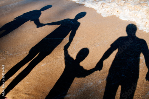 Shadows of family of four holding hands on the beach