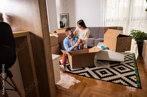 Smiling young couple move into a new home sitting on floor and unpacking.