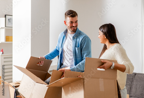 Smiling young couple move into a new home carrying boxes of belongings.