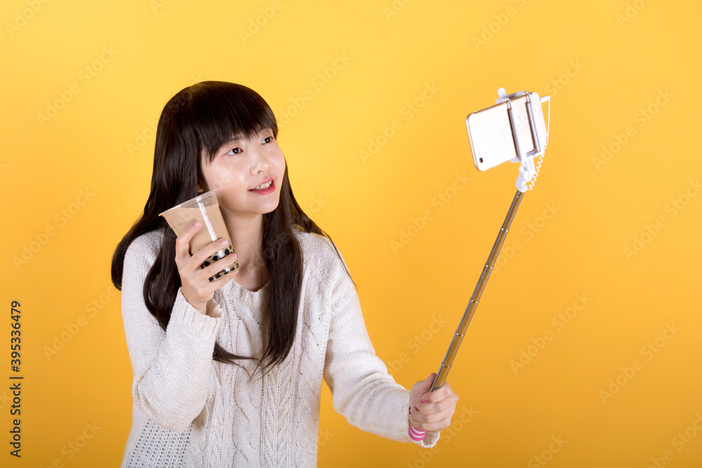 Food Vlogger streaming a live video live at studio on yellow background. Blogger holding up her phone on a selfie stick and showing pearl milk tea to fans. Food Vlogger streaming a live video live at studio on yellow background. Blogger holding up her phone on a selfie stick and showing pearl milk tea to fans.