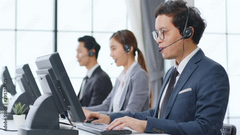 Asian call center team, customer service, telesales in formal suit wearing headset or headphone talking with customer in modern office Asian call center team, customer service, telesales in formal suit wearing headset or headphone talking with customer in modern office