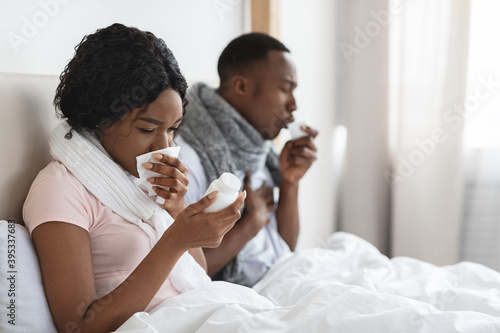 Sick couple sitting in bed, coughing and sneezing